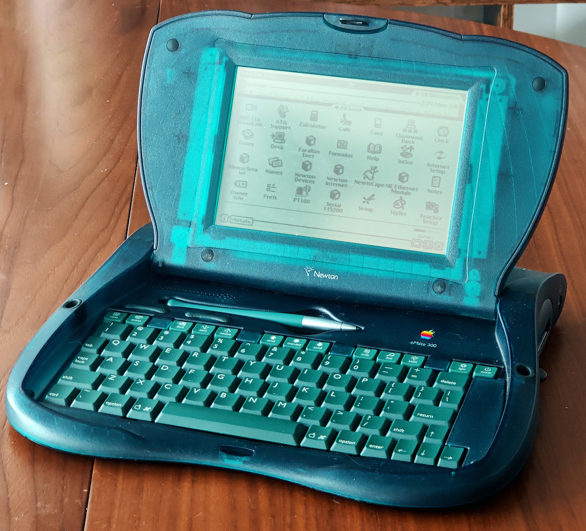 the green, oddly-shaped eMate 300, resting on a table, open and showing the home screen